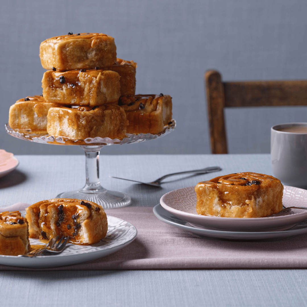 Chelsea buns with currants and syrup piled on a cake stand