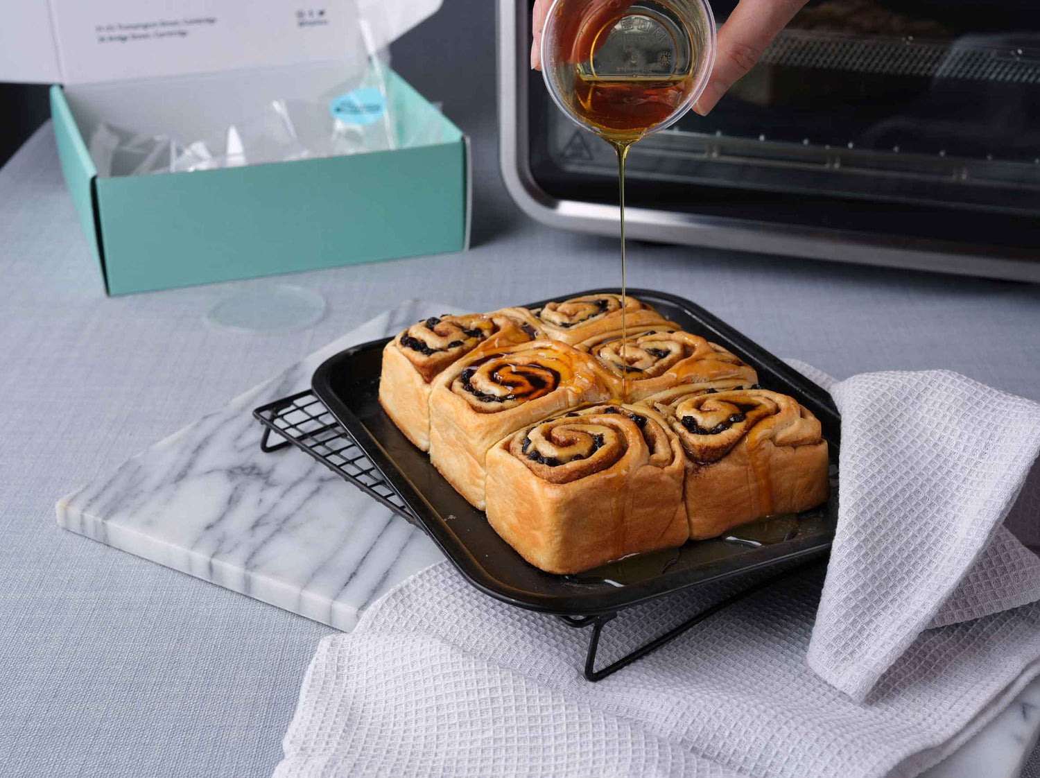 Pouring syrup over bake at home Chelsea buns cooling on an oven tray rack