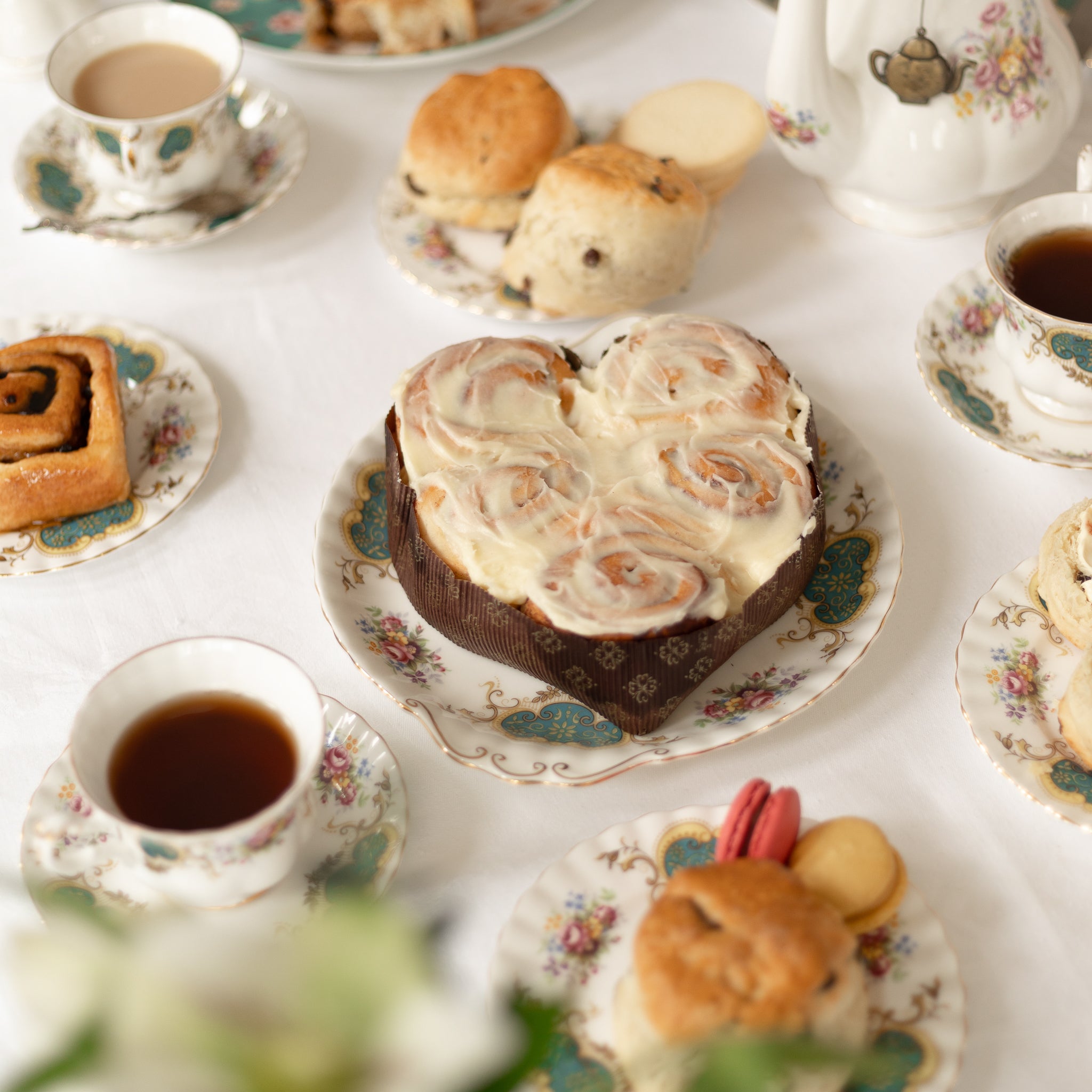 Tea party setting with pastries and teacups on a white tablecloth.